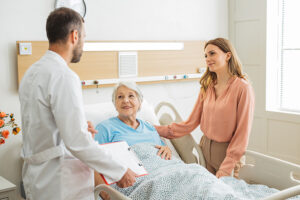 A woman and doctor support a senior in the hospital at her bedside