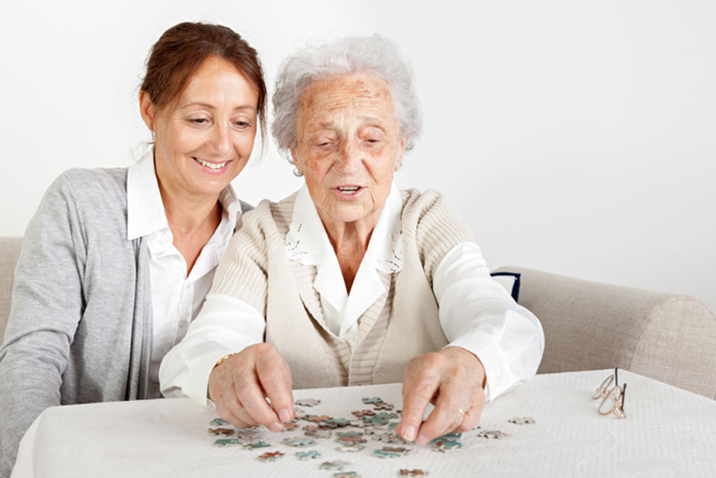 A woman does a puzzle with her elderly mother. This and other engaging activities for loved ones with dementia can help increase confidence.