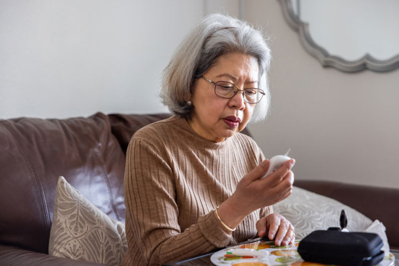 An elderly woman practices good diabetes care by checking her blood sugar levels daily.